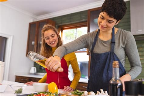 Premium Photo Happy Biracial Lesbian Couple Cooking Drizzling Oil On Chopped Vegetables In