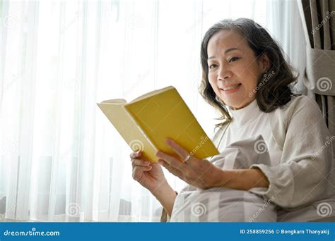 Happy Asian Middle Aged Woman Enjoys Reading A Book In The Comfortable