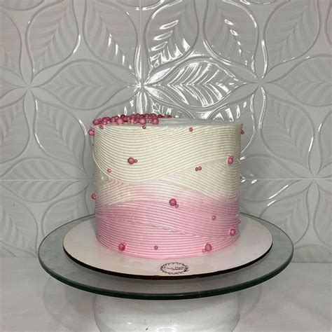 A Pink And White Cake Sitting On Top Of A Glass Plate Next To A Wall