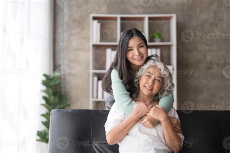 Loving Adult Daughter Hugging Older Mother Standing Behind Couch At