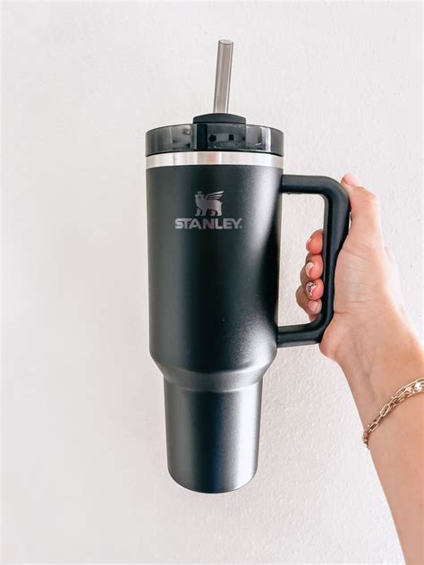 A Person Holding A Travel Mug In Their Right Hand With The Word Stanley