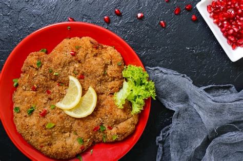 Schnitzel vienés grande sobre un plato rojo con limón sobre un fondo