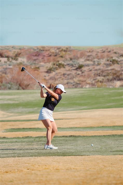 A woman swinging a golf club on a golf course photo – Golfing Image on
