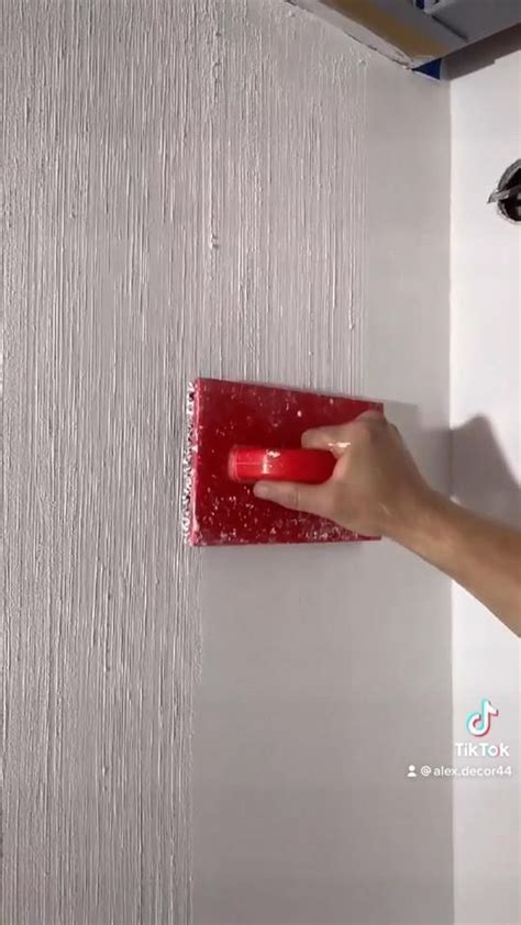 A Person Is Using A Red Brush To Paint A Wall With White Paint On It