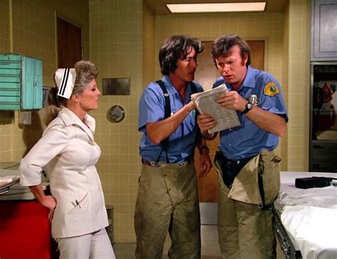 two men and a woman are standing in a hospital room looking at a clipboard