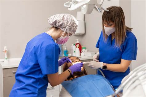 Duas mulheres dentistas dão tratamento odontológico a uma paciente de