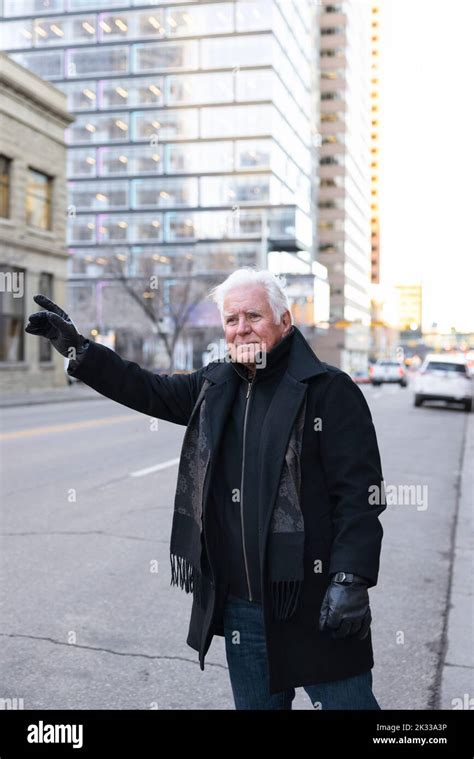 Senior Man In Winter Coat And Gloves Hailing A Taxi On City Street