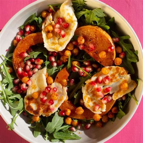 A White Bowl Filled With Food On Top Of A Pink Tablecloth Covered In Pomegranate