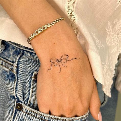 A Woman S Hand With A Small Bow Tattoo On Her Left Wrist And The Word