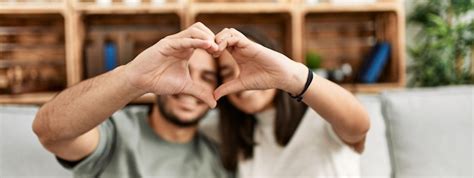 Joven pareja latina sonriendo feliz haciendo el símbolo del corazón con