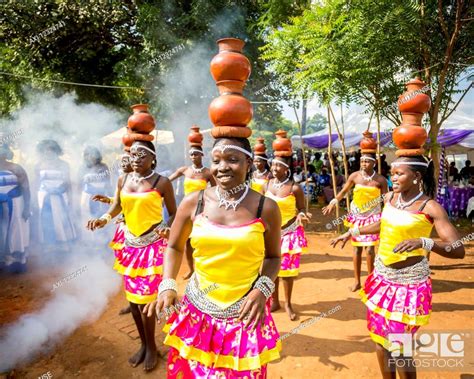 Women wearing brightly coloured traditional clothing walk and carry pottery on their heads ...