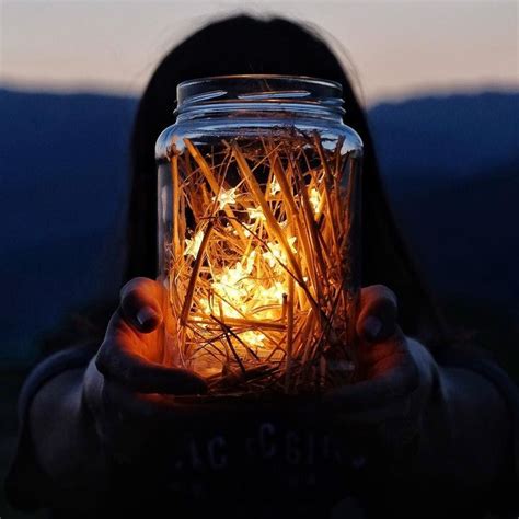 A Person Holding A Mason Jar Filled With Sticks And Glowing Lights In