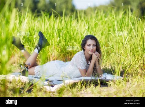 Young Blonde Woman In White Dress Lies On A Picnic Sheet In Tall Grass