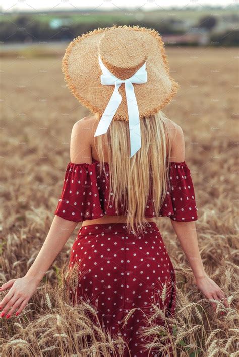 A Woman Wearing A Straw Hat Standing In A Field With Her Hands Behind Her Back