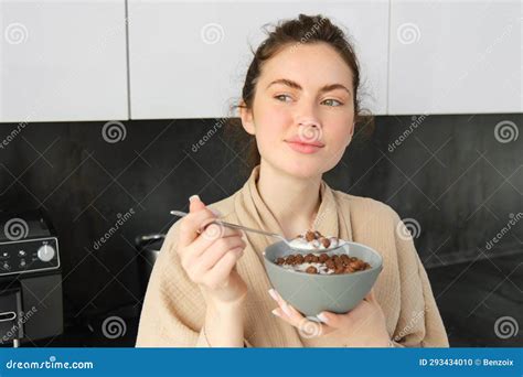 Good Looking Brunette Woman Eating Her Breakfast Standing In Kitchen Near Worktop And Holding