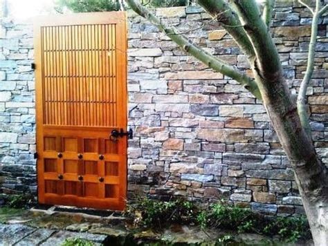 An Orange Wooden Door In Front Of A Brick Wall Next To A Tree And Stone