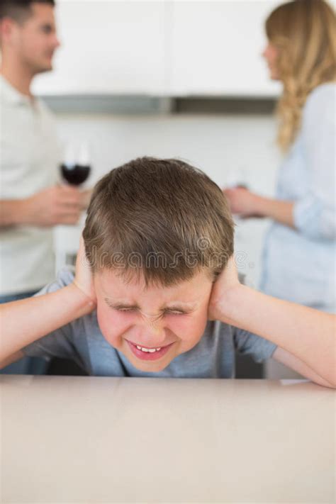 Unhappy Siblings Sitting In Kitchen With Their Parents Who Are A Stock