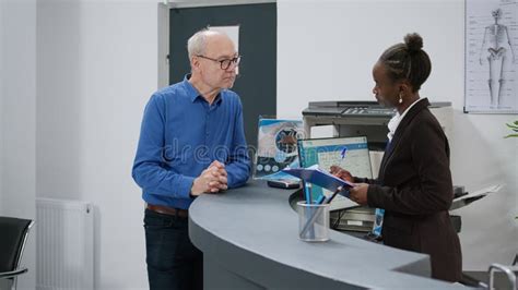 Patient Talking To Female Receptionist Before Attending Appointment