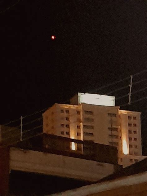 An Apartment Building Lit Up At Night With The Moon In The Sky Behind