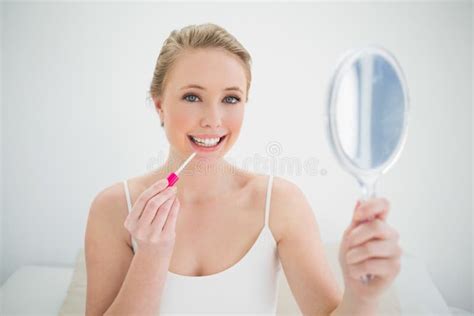 Natural Smiling Blonde Holding Mirror And Applying Lip Gloss Stock