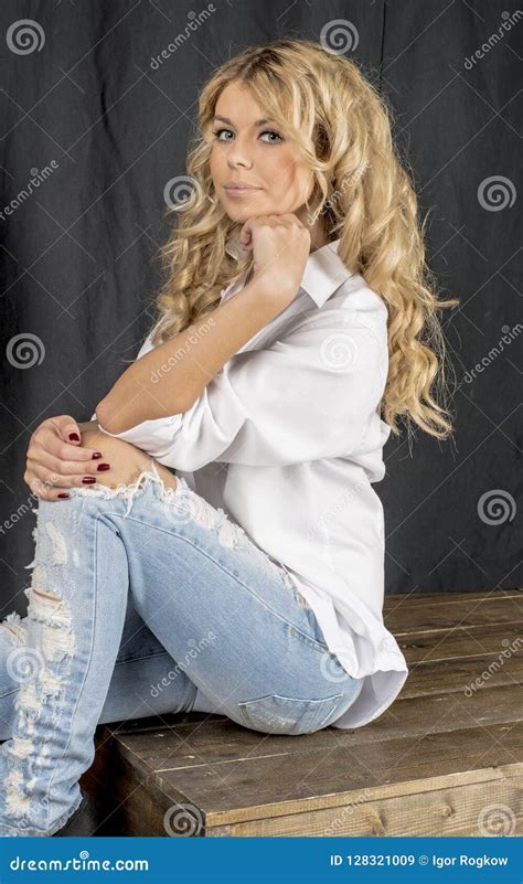 Blonde Hermoso Joven De La Muchacha En Una Camisa Blanca Y Vaqueros Con Huecos Imagen De Archivo