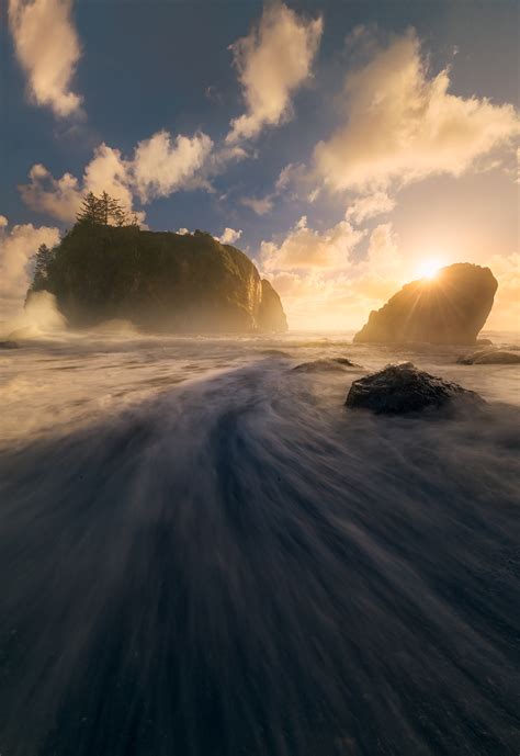 A Sun Star Peaking Over A Sea Stack Along The Coastline At Olympic