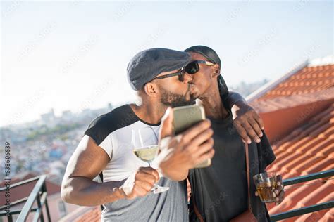 Portrait Of Romantic African Gay Couple Kissing For Selfie Two Handsome Men Standing On Balcony