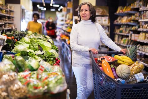 Elderly Woman Walking With Shopping Trolley In Grocery Shop Stock Image