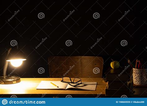 Table Lamp Desk Notebook And Books Next To Chair In Dark Room