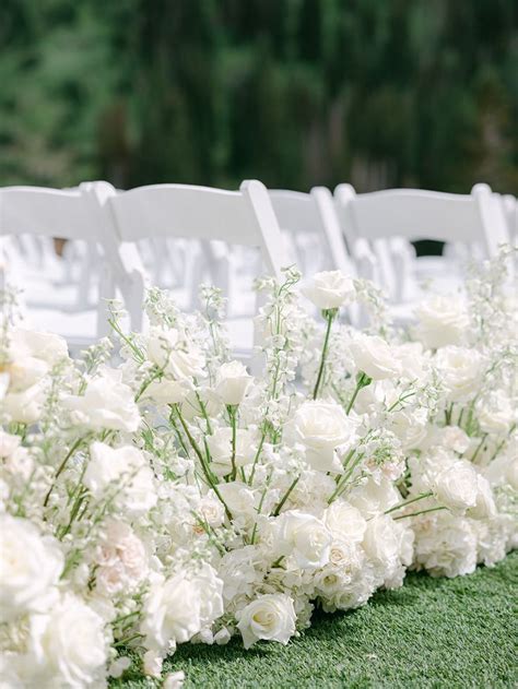 Rows Of White Chairs Lined Up With Flowers On The Grass At An Outdoor