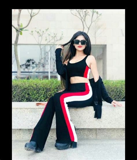 A Woman Sitting On Top Of A Stone Wall Wearing Black And Red Pants With