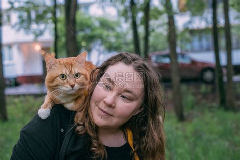 一个女人带着一只猫在公园里散步猫坐在他的肩膀上小女孩在房子附近的绿色公园里散步高清图片下载 正版图片506679670 摄图网