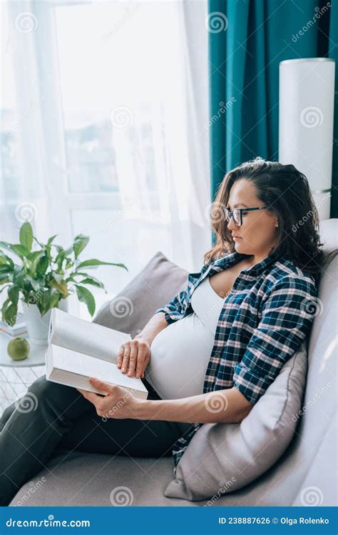 Middle Age Brunette Pregnant Woman In Glasses Read Book Sitting On Grey