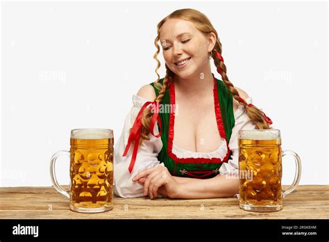 Beautiful redhead woman wearing folk German dirndl looking at two beer ...