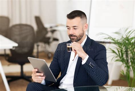 Serious Confident Caucasian Mature Guy In Suit Drinking Cup Of Coffee Chatting On Tablet For