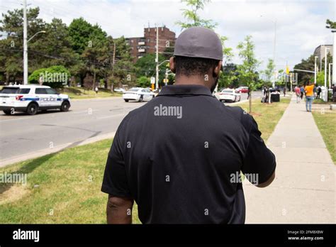 Black Security Guard In Uniform Patrolling A Wide Street In The Daytime