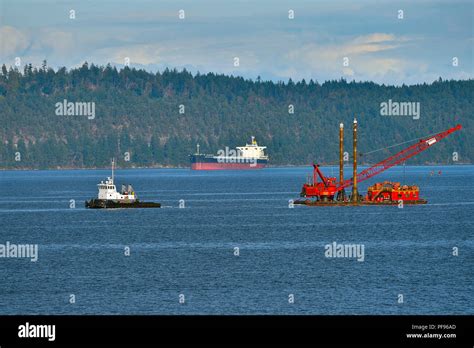 A Tug Boat Pulling A Heavy Barge With A Crane Onboard Through The