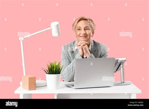 Mature Female Programmer Working With Laptop At Table On Pink