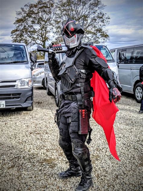 A Man Dressed In Black And Red Standing Next To A Silver Van With A Red