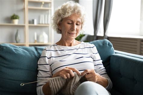 Satisfied Older Woman Knitting Sitting On Sofa At Home Stock Image