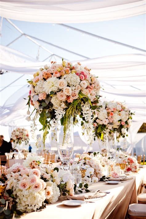 A Table Topped With Lots Of Flowers Next To Tall Vases Filled With