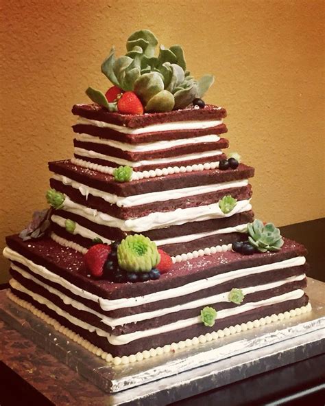 A Very Tall Cake Sitting On Top Of A Table With Succulents And Strawberries