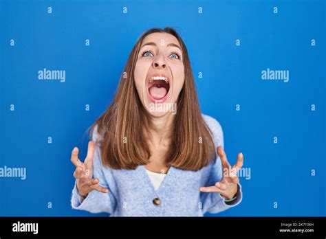 Young Woman Standing Over Blue Background Crazy And Mad Shouting And Yelling With Aggressive