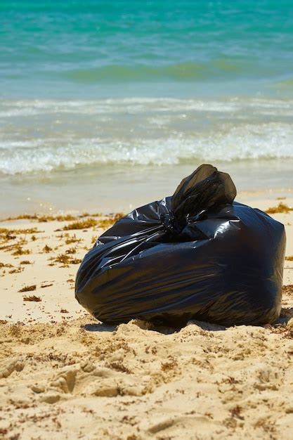 Sac Poubelle En Plastique Noir Sur Une Plage De Sable Avec Une Mer