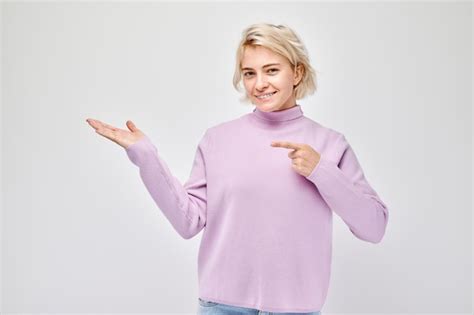 Junge blonde Frau in Casual Kleidung hält etwas in der Hand und zeigt leeren Raum für Produkt