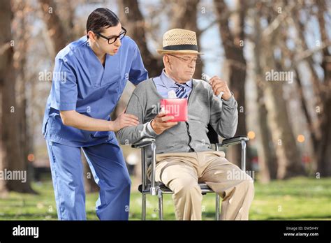 Young Male Doctor Comforting A Sad Senior Man Seated In A Wheelchair In