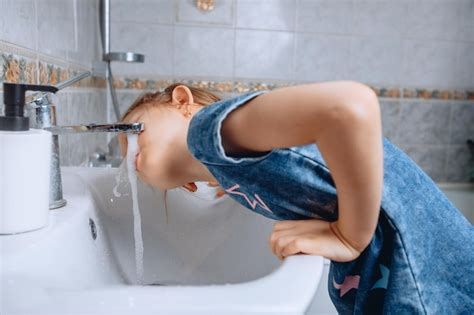 Uma Garotinha De Vestido Jeans Estampa Se Inclinou Sobre Uma Pia De