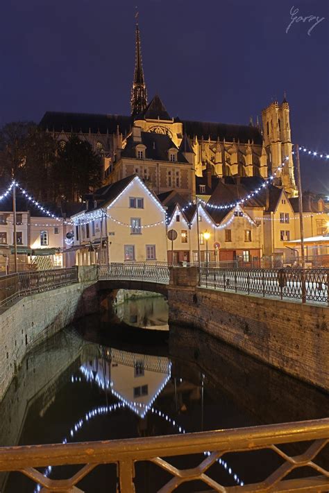 A Bridge Over A River With Buildings In The Background And Lights