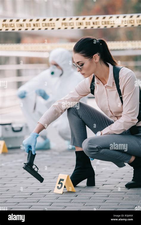 Female Detective Taking Gun As A Clue With Criminologist Behind Her At