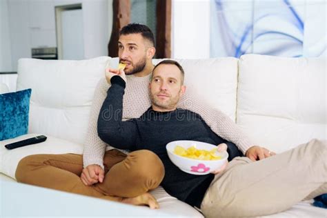 Casal Gay Sentado No Sofá Em Casa Assistindo Algo Na Tv E Tendo Um Lanche Imagem de Stock